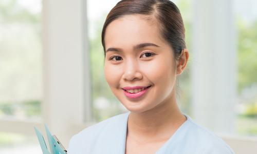 Medical Assistant Holding Clipboard Smiling in Hallway 