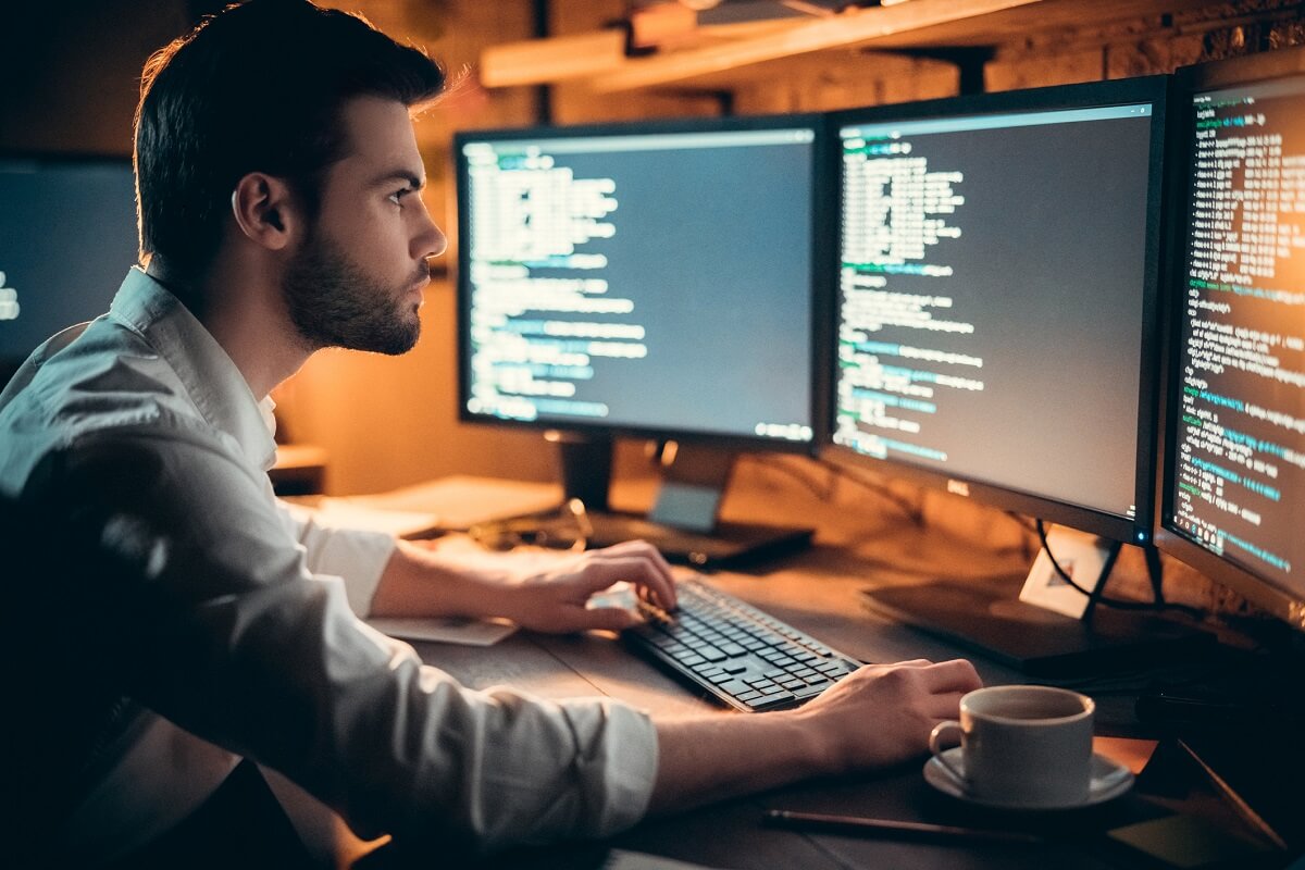 Programmer Coding on Computer with Three Monitors