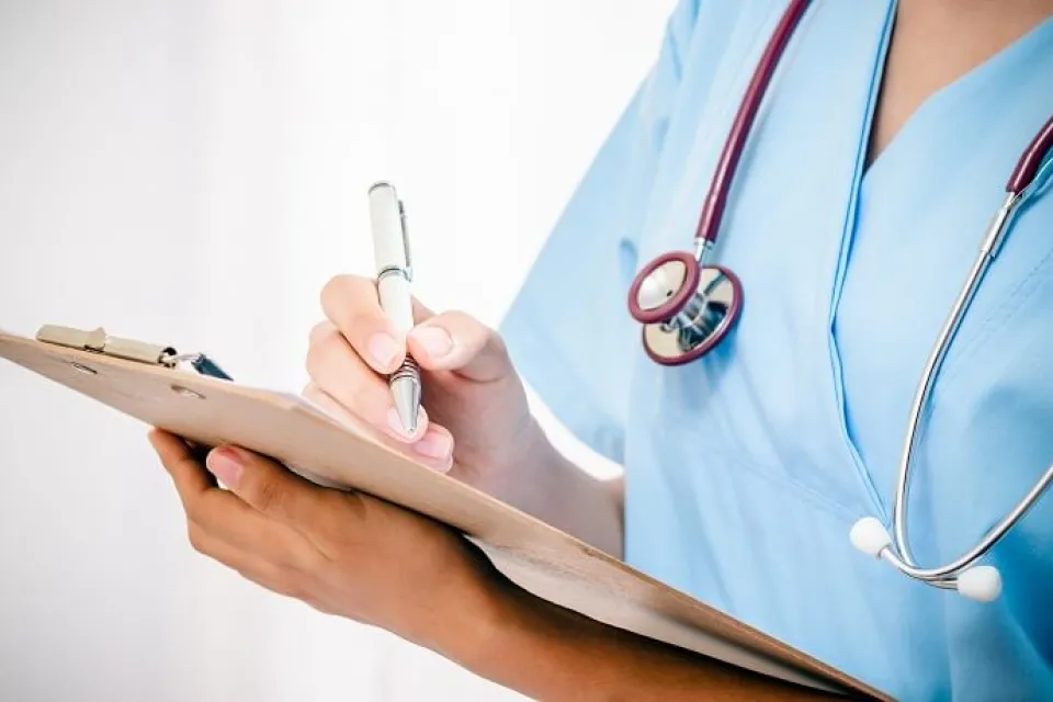 Practical Nurse LPN in Blue Scrubs Taking Notes on Clipboard