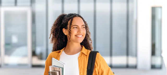 Student wearing backpack and smiling holding textbook